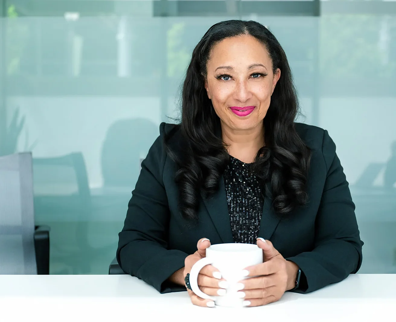 Dhorea Ramanula seated at a table, holding a mug and smiling toward the camera